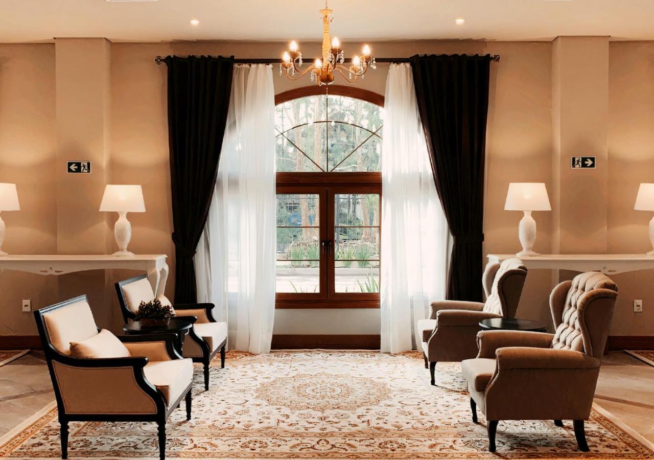 Buona Vitta Gramado Resort & Spa By Gramado Parks ภายนอก รูปภาพ The photo shows an elegantly styled living room. There are two armchairs and a sofa arranged comfortably around an intricate area rug. Large windows are adorned with sheer white curtains and dark curtains, allowing natural light to fill the space. A 