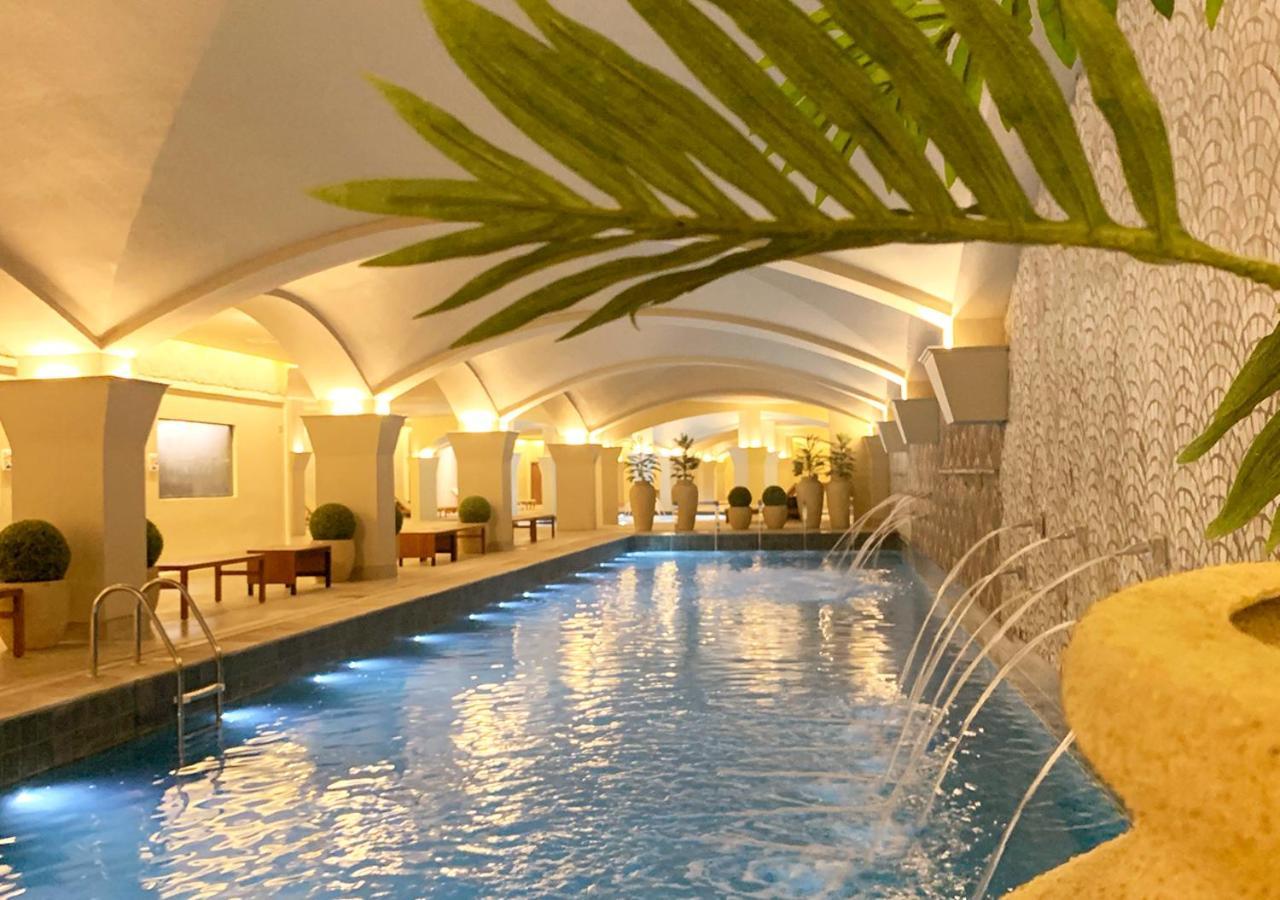 Buona Vitta Gramado Resort & Spa By Gramado Parks ภายนอก รูปภาพ The photo shows an indoor swimming pool with a serene and elegant atmosphere. The pool has a calm blue water surface, illuminated by soft lights along its edges. The architectural design features arches in the ceiling, creating an open and spacious f