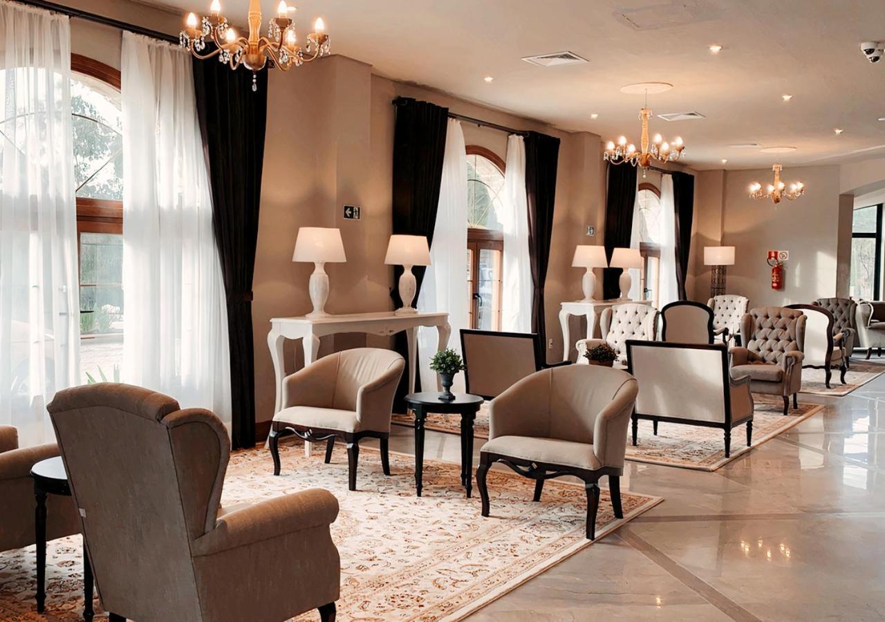 Buona Vitta Gramado Resort & Spa By Gramado Parks ภายนอก รูปภาพ The photo depicts a stylish and sophisticated lounge area. It features several elegant chairs and sofas, arranged around small tables on a decorative rug. The room is well-lit with natural light coming in through large windows dressed with flowing wh