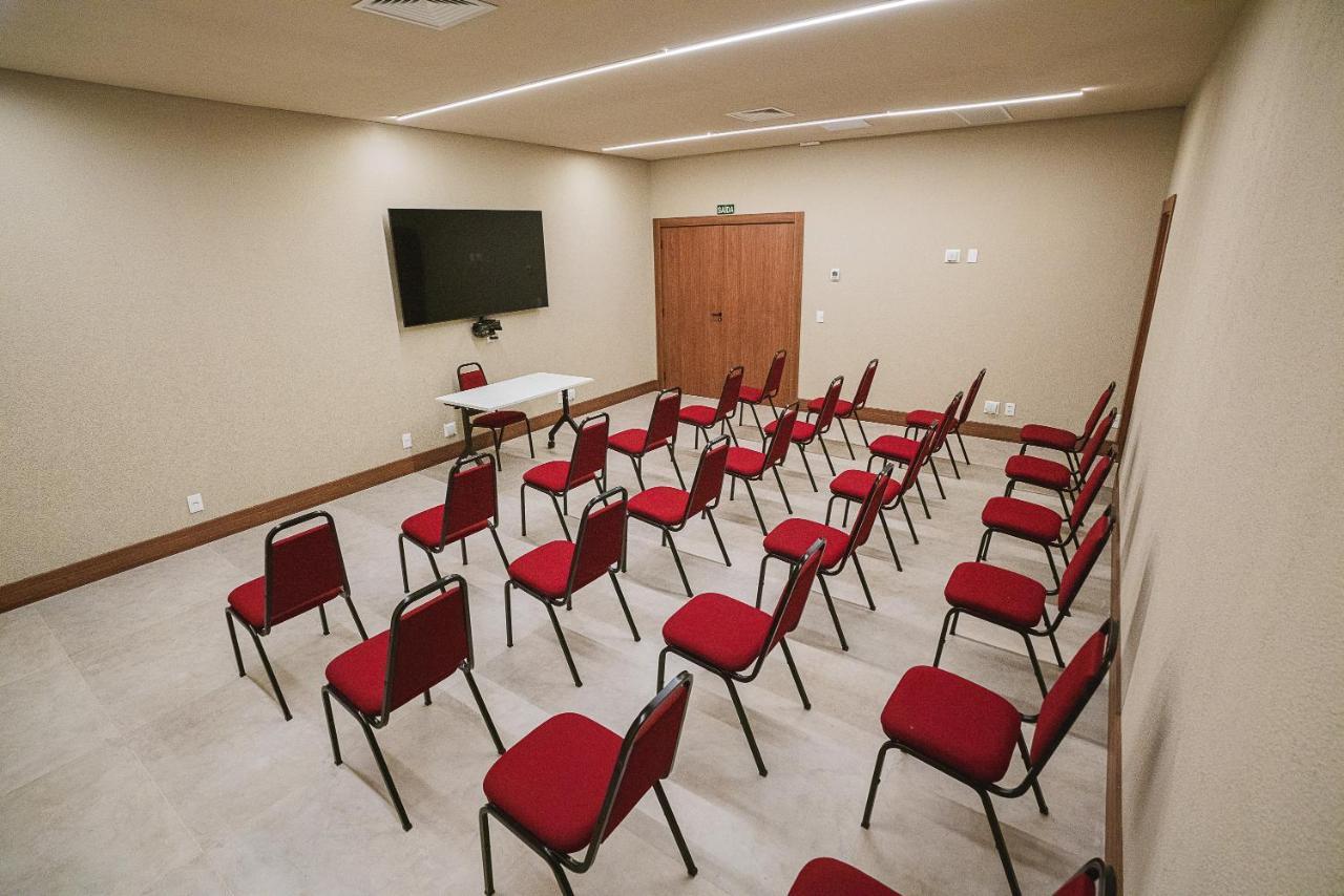 Buona Vitta Gramado Resort & Spa By Gramado Parks ภายนอก รูปภาพ The photo shows a conference or meeting room with a simple and modern design. There are several rows of red chairs arranged in a semi-circle facing a white table at the front. On the wall opposite the chairs, there is a flat-screen television mounted