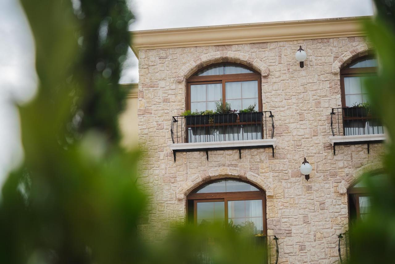 Buona Vitta Gramado Resort & Spa By Gramado Parks ภายนอก รูปภาพ The photo depicts a stone building with a textured exterior. It features several windows with wooden frames. Each window has a small balcony adorned with decorative plants. There are also wall-mounted light fixtures flanking the windows. In the foreg