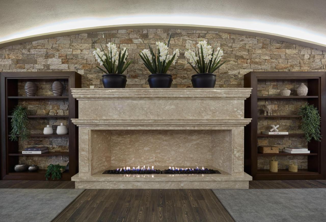 Buona Vitta Gramado Resort & Spa By Gramado Parks ภายนอก รูปภาพ The photo shows a modern fireplace design built into a wall with a textured stone background. The fireplace is made of a light-colored stone and features a long, narrow gas flame visible at the bottom. Above the fireplace, there are two large potted 