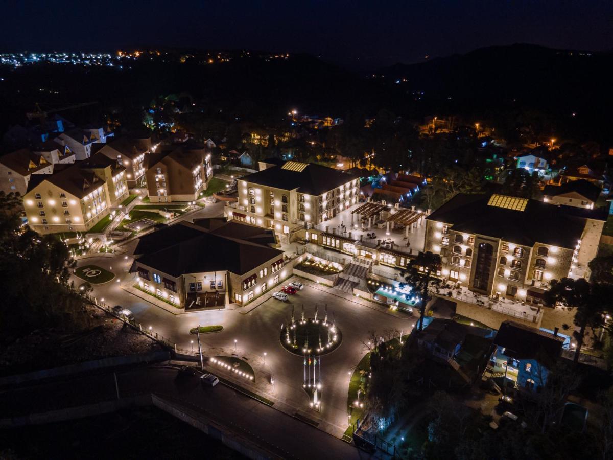 Buona Vitta Gramado Resort & Spa By Gramado Parks ภายนอก รูปภาพ The photo shows a beautifully lit resort or hotel complex taken at night. The buildings are well-illuminated, highlighting their architecture. There is a circular area with a fountain at the center, surrounded by pathways that connect various parts o