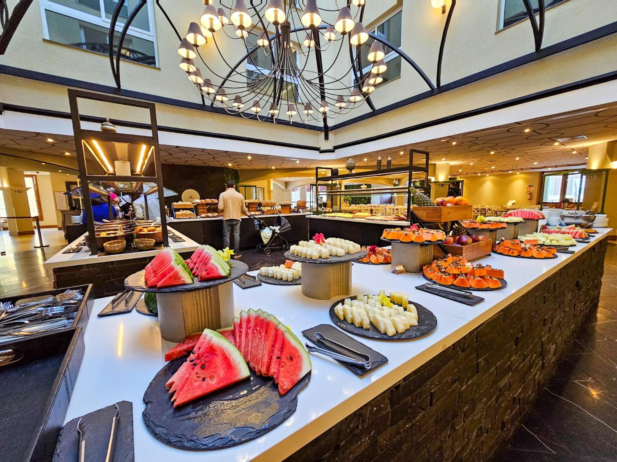 Buona Vitta Gramado Resort & Spa By Gramado Parks ภายนอก รูปภาพ The photo depicts a lavish buffet setup in a dining area. In the foreground, there are several platters featuring an assortment of colorful food items, primarily fruits like watermelon and various types of sushi or rolls. The buffet table is elegantl