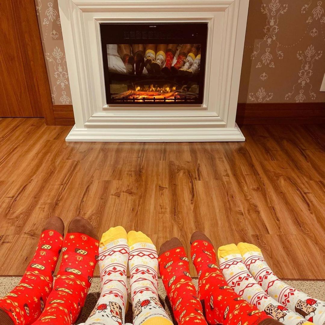 Buona Vitta Gramado Resort & Spa By Gramado Parks ภายนอก รูปภาพ The photo shows a cozy indoor setting with a warm fireplace. In the foreground, several pairs of feet are displayed, each wearing brightly colored socks with various patterns. The socks include red, yellow, and white designs, contributing to a cheerf
