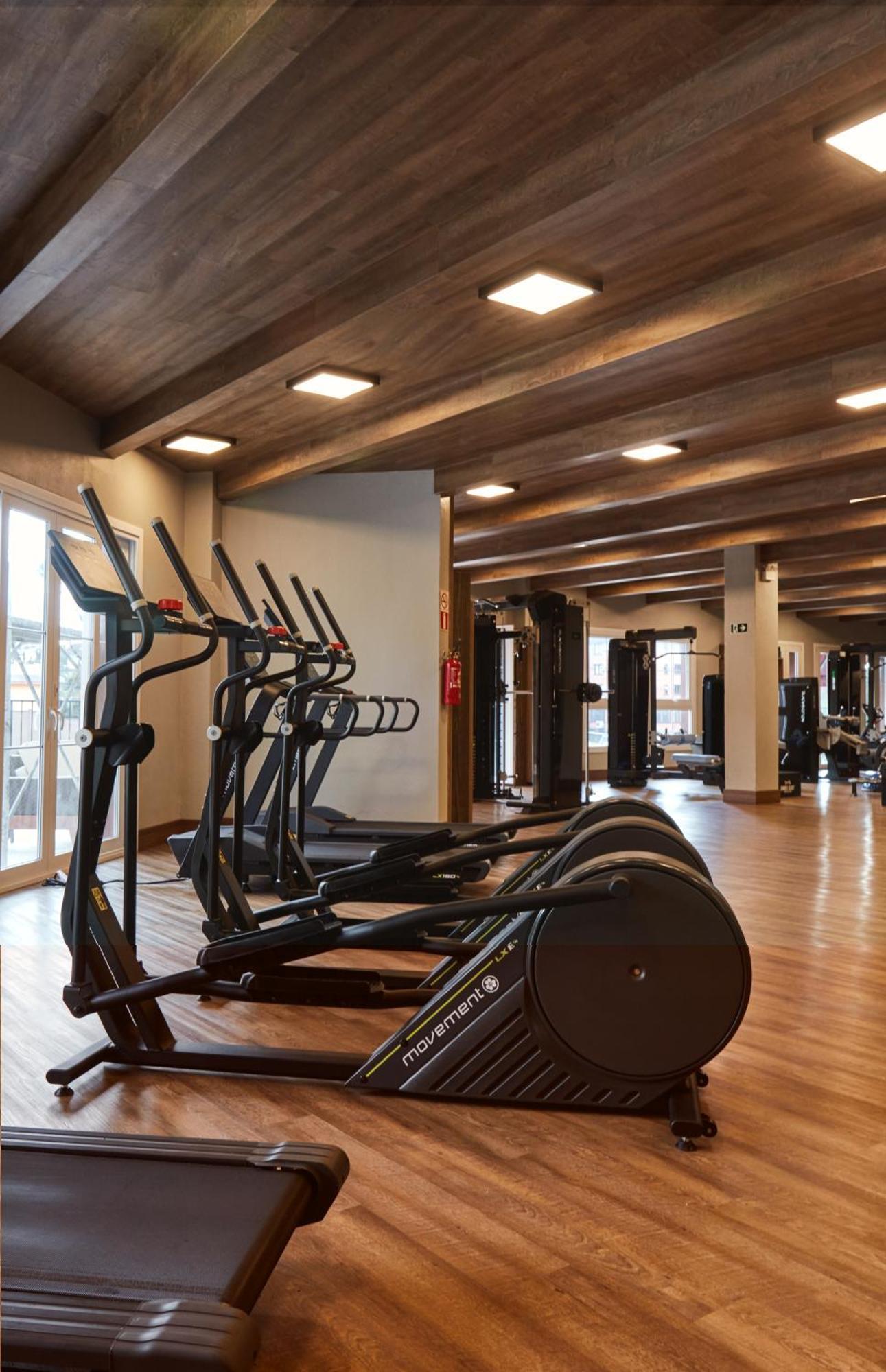 Buona Vitta Gramado Resort & Spa By Gramado Parks ภายนอก รูปภาพ The photo shows a modern gym interior with wooden flooring and a ceiling with wooden beams. There are several exercise machines, including elliptical trainers and a treadmill, positioned in the foreground. In the background, there are additional work