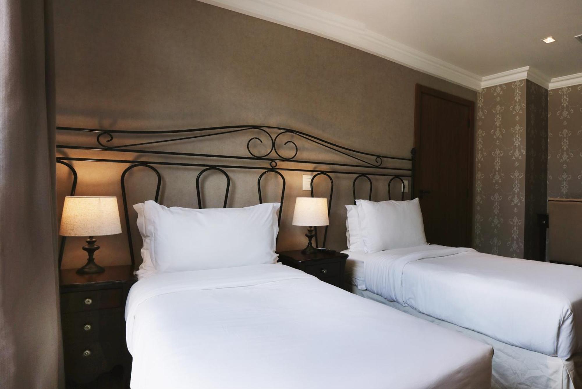 Buona Vitta Gramado Resort & Spa By Gramado Parks ภายนอก รูปภาพ The photo shows a neatly arranged hotel room featuring two single beds with white bedding. The beds have decorative metal headboards, and there are bedside tables on either side with lamps. The room's walls have a subtle design, and there is a door v