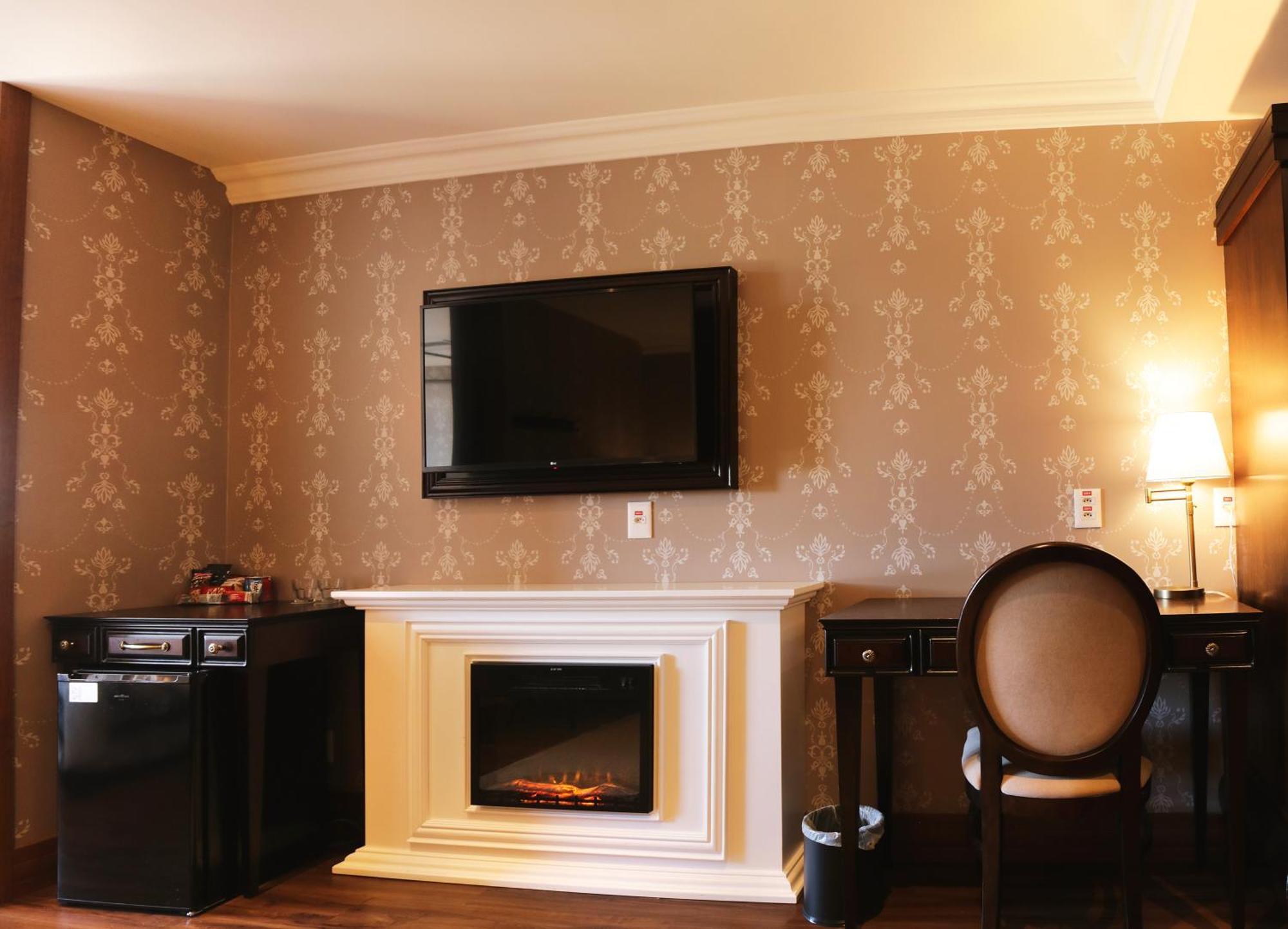 Buona Vitta Gramado Resort & Spa By Gramado Parks ภายนอก รูปภาพ The photo shows a cozy room featuring a decorative wall with a subtle pattern. On one side, there is a modern flat-screen television mounted on the wall. Below it, there is a stylish electric fireplace framed in white. Adjacent to the fireplace is a 