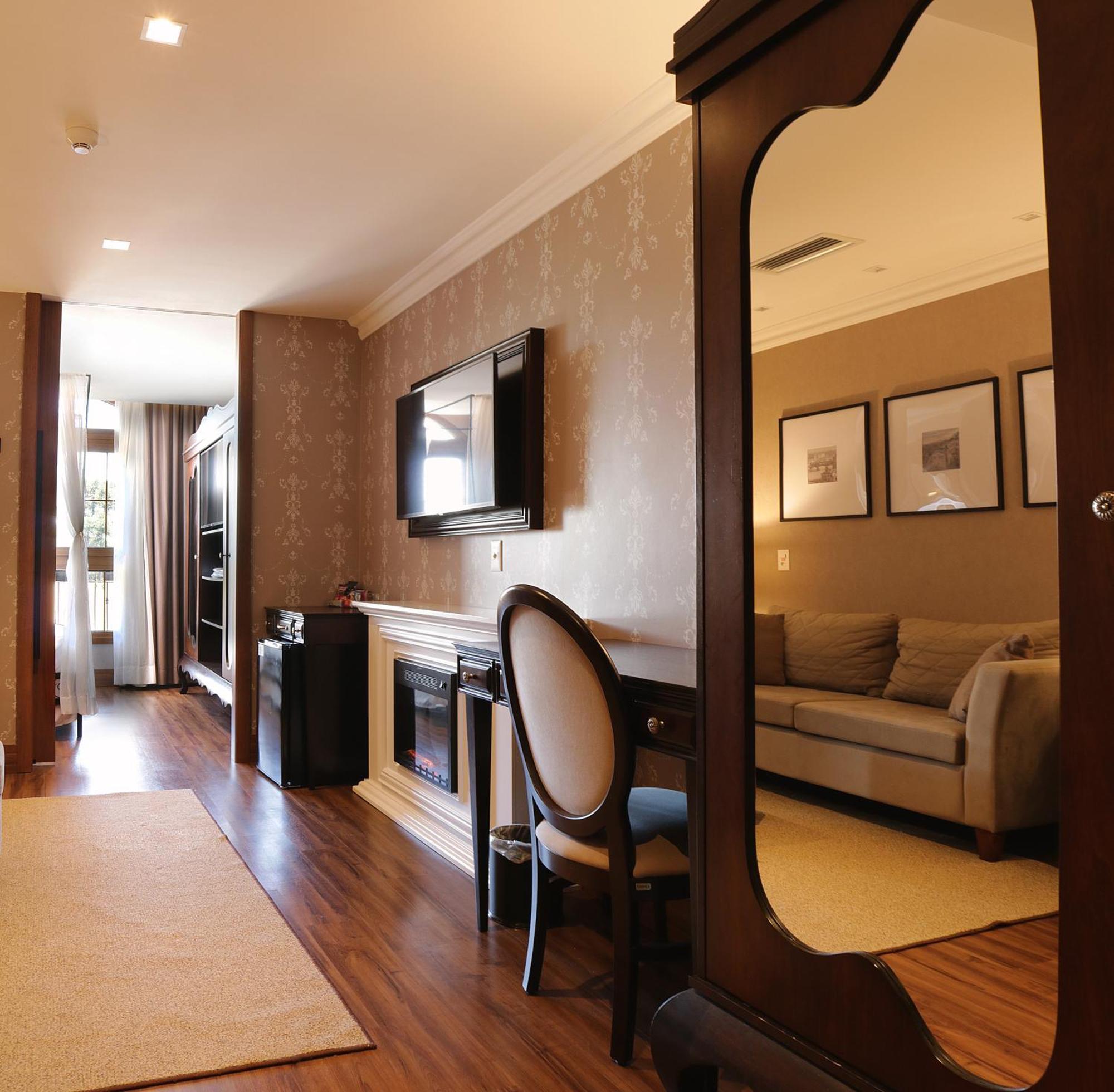 Buona Vitta Gramado Resort & Spa By Gramado Parks ภายนอก รูปภาพ The photo shows a well-decorated room that appears to be a living area or a hotel suite. In the foreground, there is a round chair and a desk. A large mirror reflects the living space, creating a sense of spaciousness. 

On the wall is a flat-screen 
