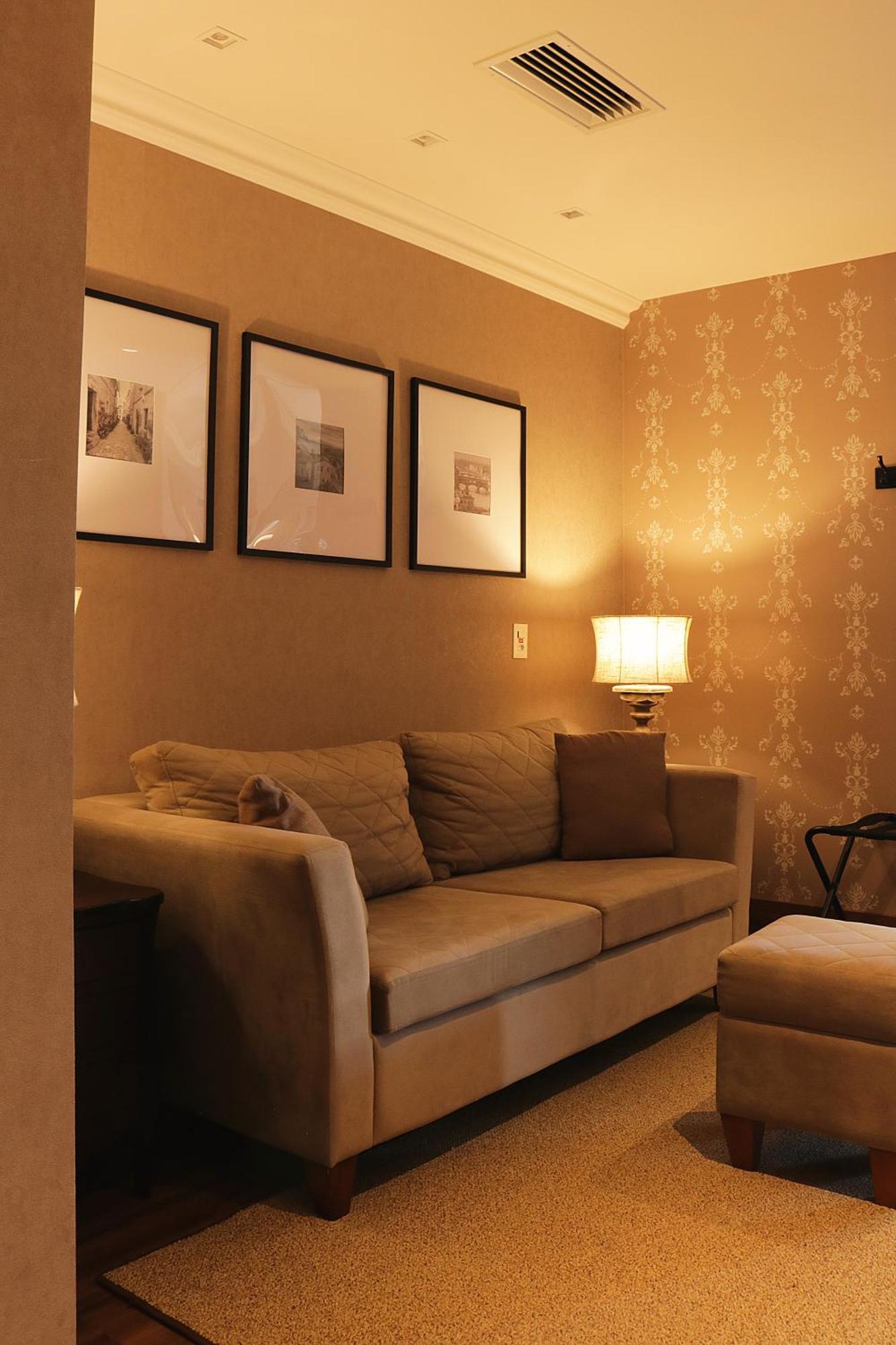 Buona Vitta Gramado Resort & Spa By Gramado Parks ภายนอก รูปภาพ The photo shows a cozy living room setting. There is a light-colored sofa adorned with several cushions, positioned against a wall that has a subtle pattern. Above the sofa, there are three framed artworks or photographs hanging on the wall. To the s