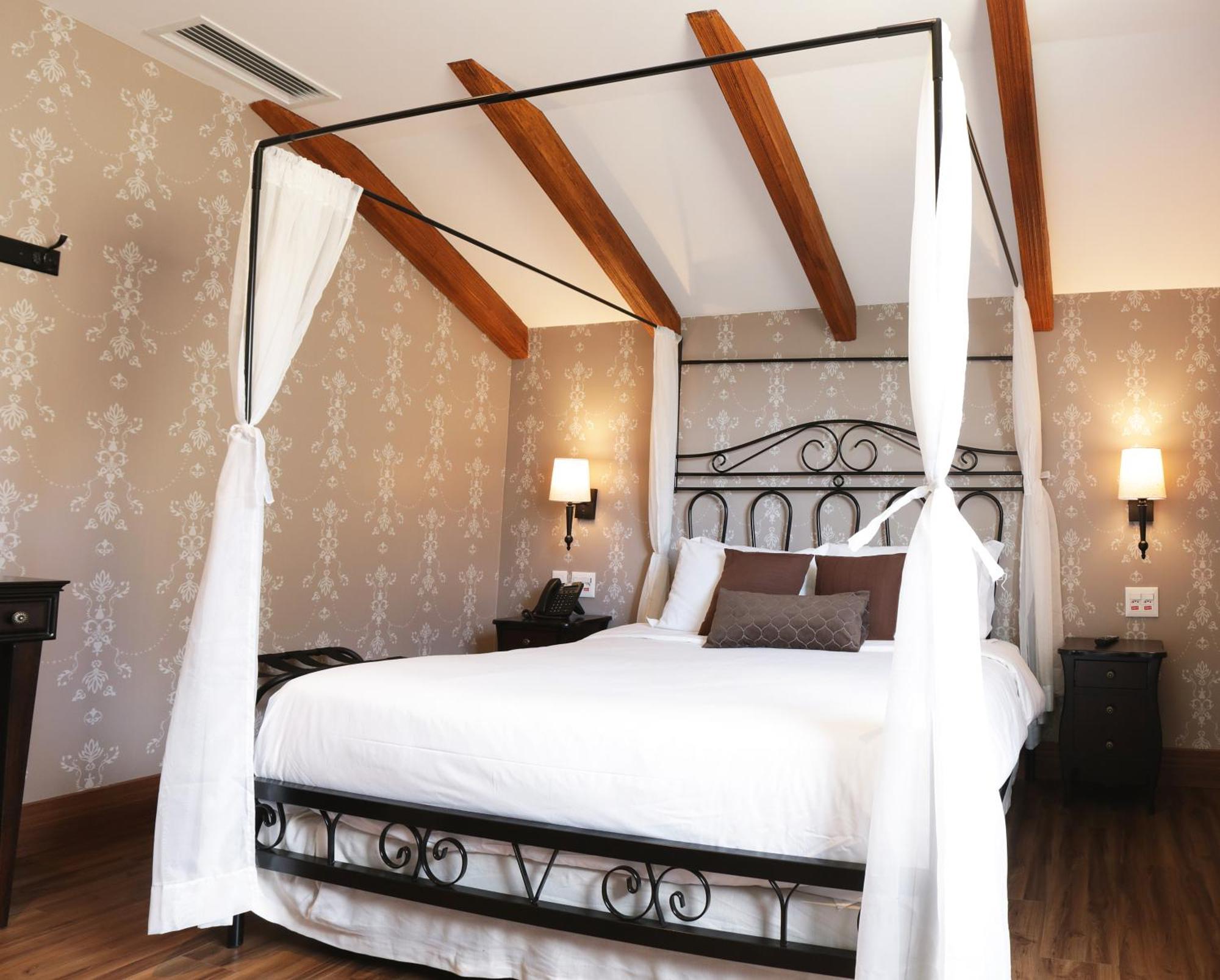 Buona Vitta Gramado Resort & Spa By Gramado Parks ภายนอก รูปภาพ The photo shows a beautifully designed bedroom featuring a four-poster bed with a metal frame and flowing white curtains. The bed is adorned with white bedding and brown decorative pillows. The room has wooden beams on the ceiling and is decorated wi