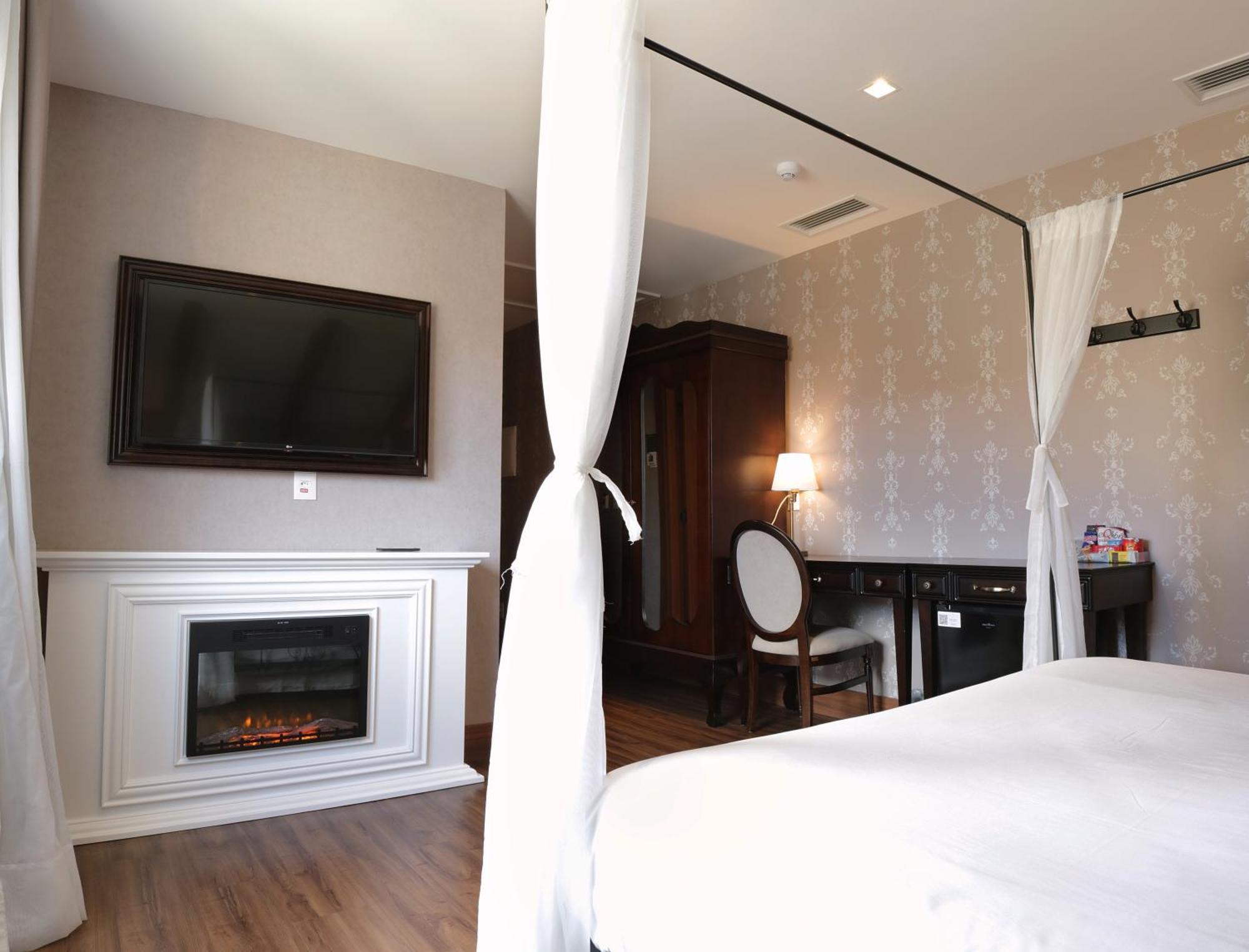 Buona Vitta Gramado Resort & Spa By Gramado Parks ภายนอก รูปภาพ The photo shows a cozy hotel room with elegant decor. There is a white bed with a canopy, and a modern television mounted on the wall across from it. To the side, a fireplace is built into a white mantel, adding a warm touch to the space. There's a w